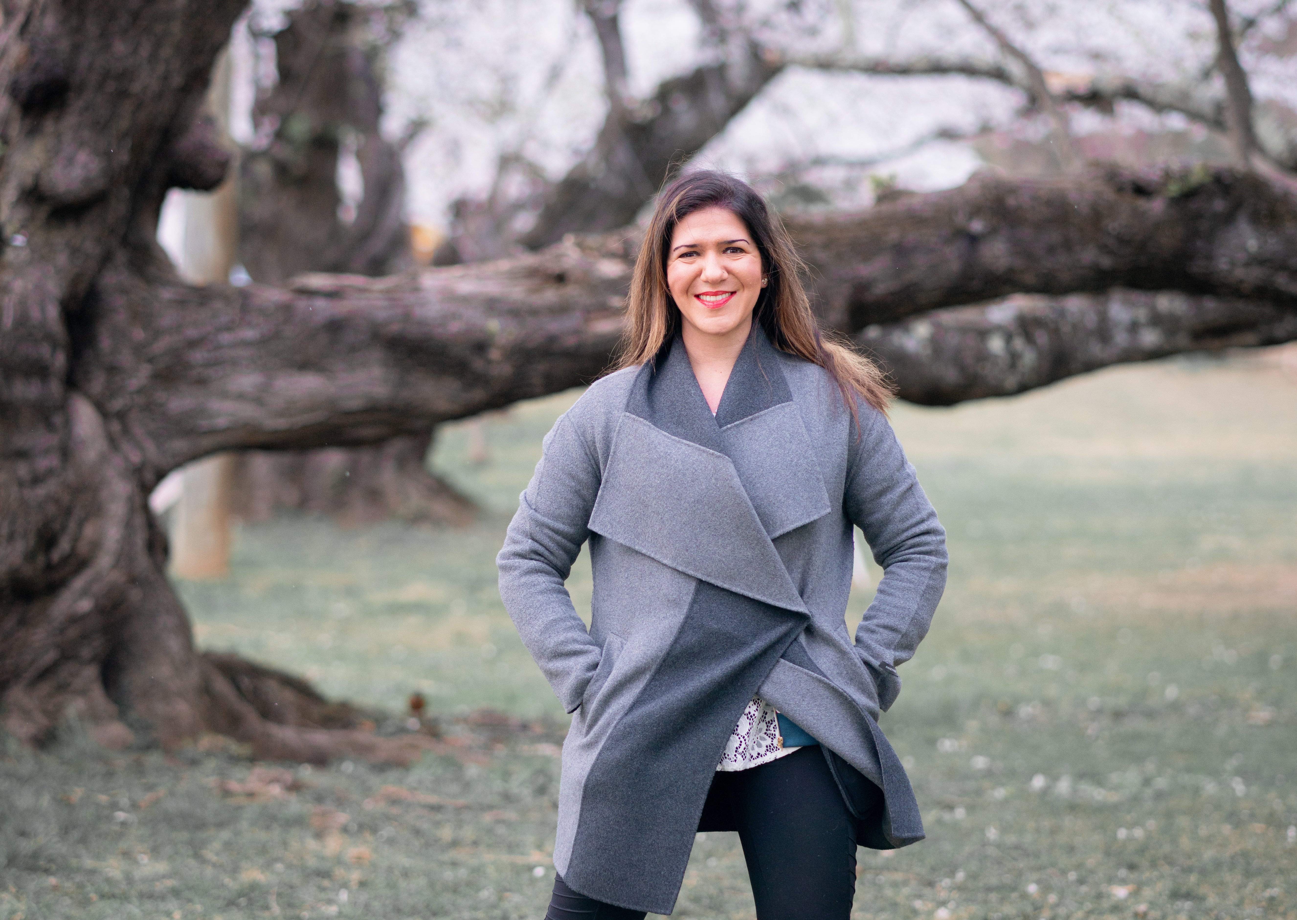 Photograph of Lauren, a white woman with long brown hair, standing in front of a tree wearing a grey coat.