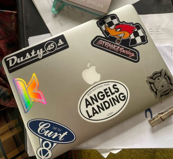 StrangeMama's laptop with a Kanopi sticker and various other decals