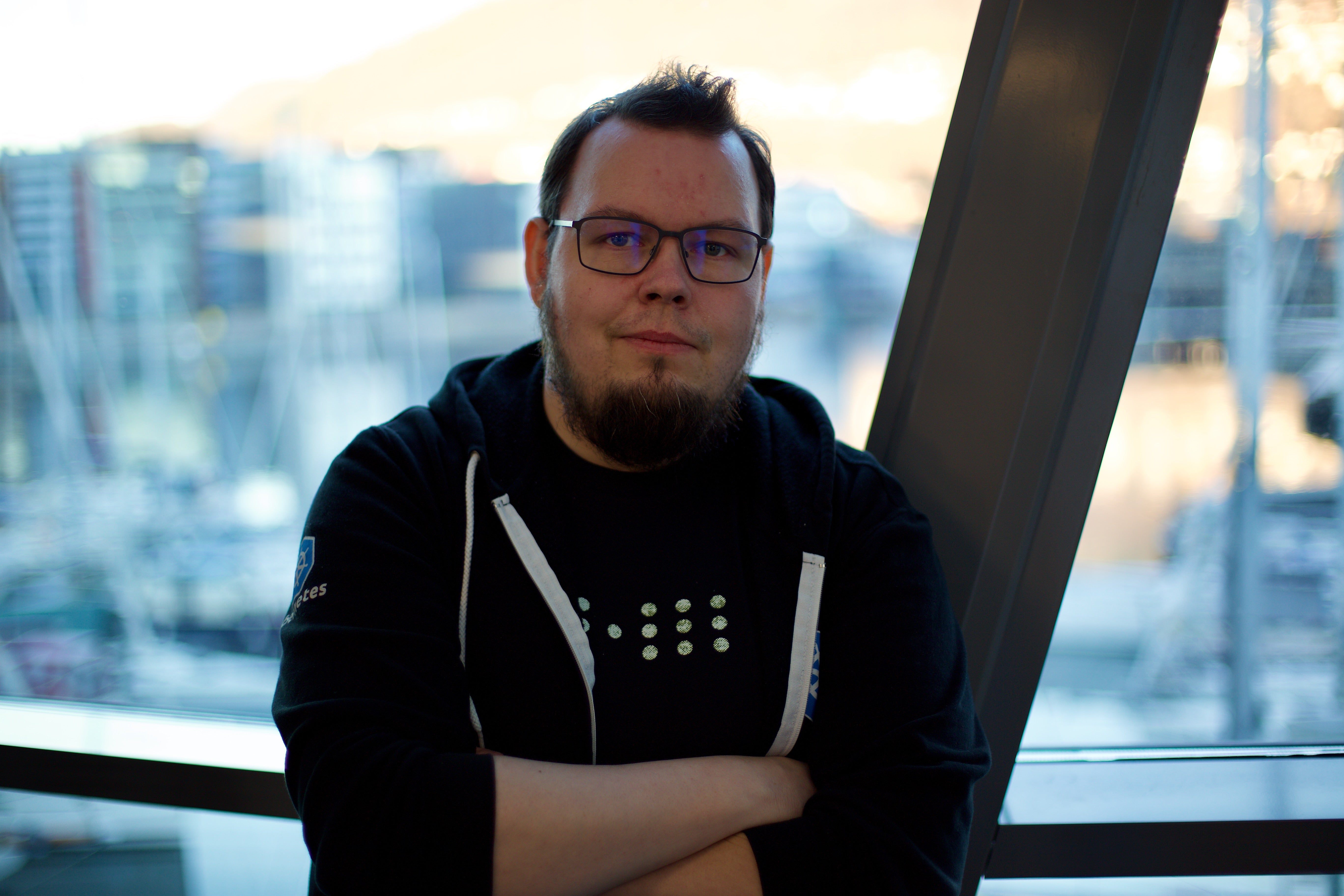 Roberth Strand, standing in front of a window, wearing a Kubernetes hoodie and his company t-shirt
