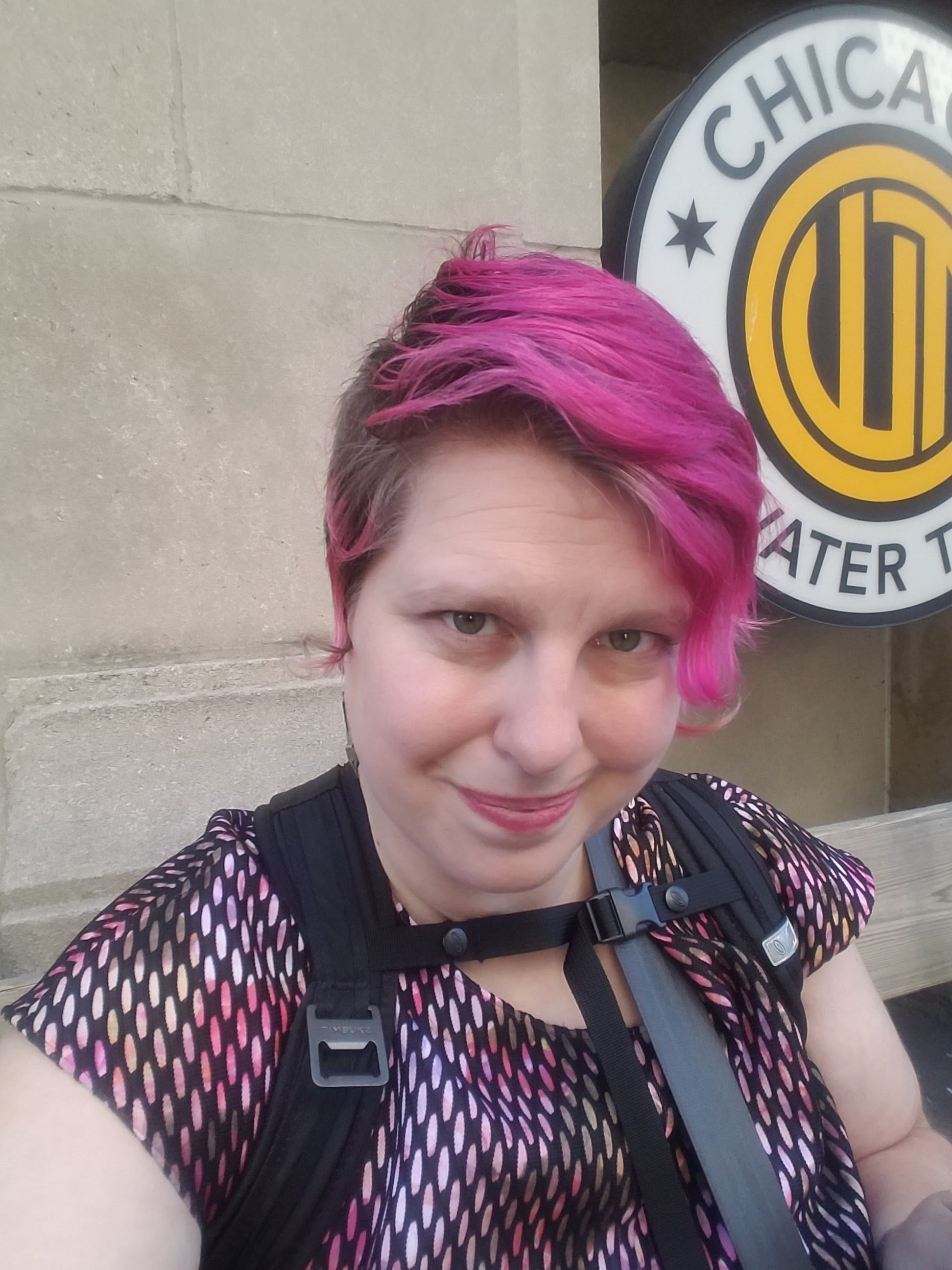 A pink-haired woman with a half-smile looks directly into the camera.