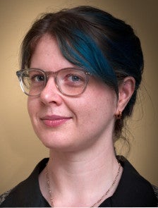 A slightly old photo of Molly de Blanc, in which she has blue highlights in her hair. She is wearing a black shirt and clear glasses.
