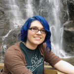 Emilie Nouveau with blue hair in front of waterfall