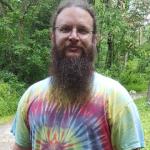 Tie dye wearing hippie Matthew with a long beard hiking in the woods.