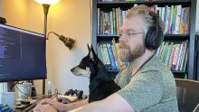 bearded bespectacled guy and small dog seated & looking at a computer