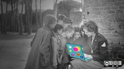 Group of kids crowded around a teacher with a laptop
