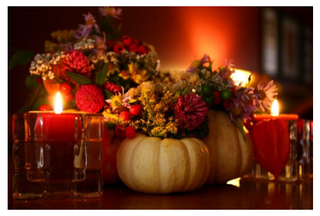A candlelight centerpiece using pumpkin shells as flower holders for small red and yellow floral bouquets.