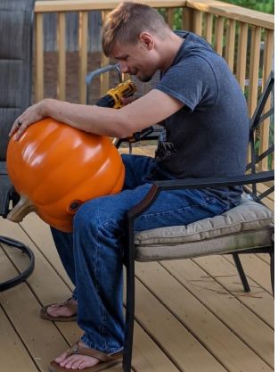A man drilling a hole in the bottom of a large plastic jack o'lantern
